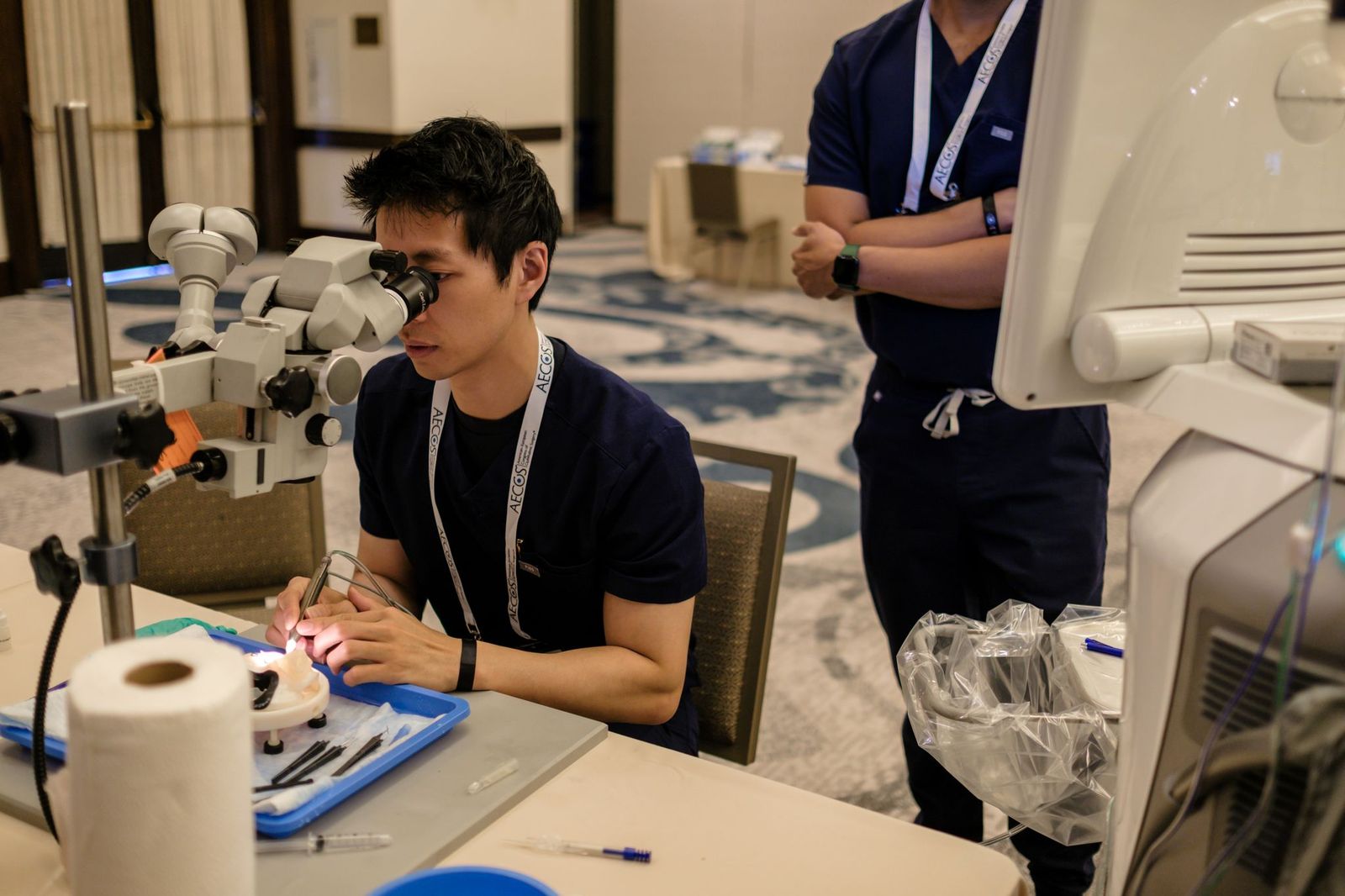 A resident practicing microsurgery at a wet-lab station while a colleague observes