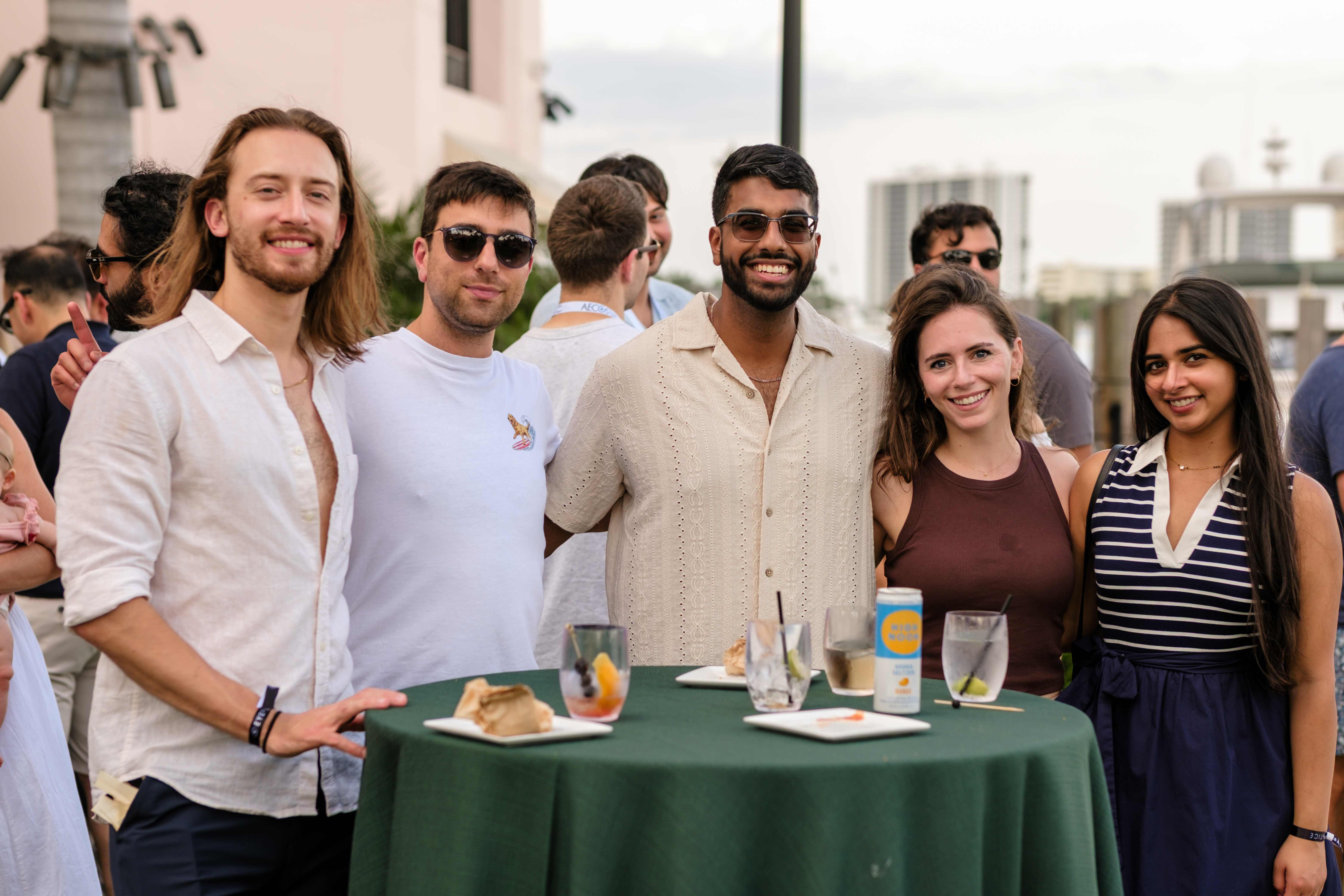 Attendees gathered around a cocktail table at a rooftop reception at dusk
